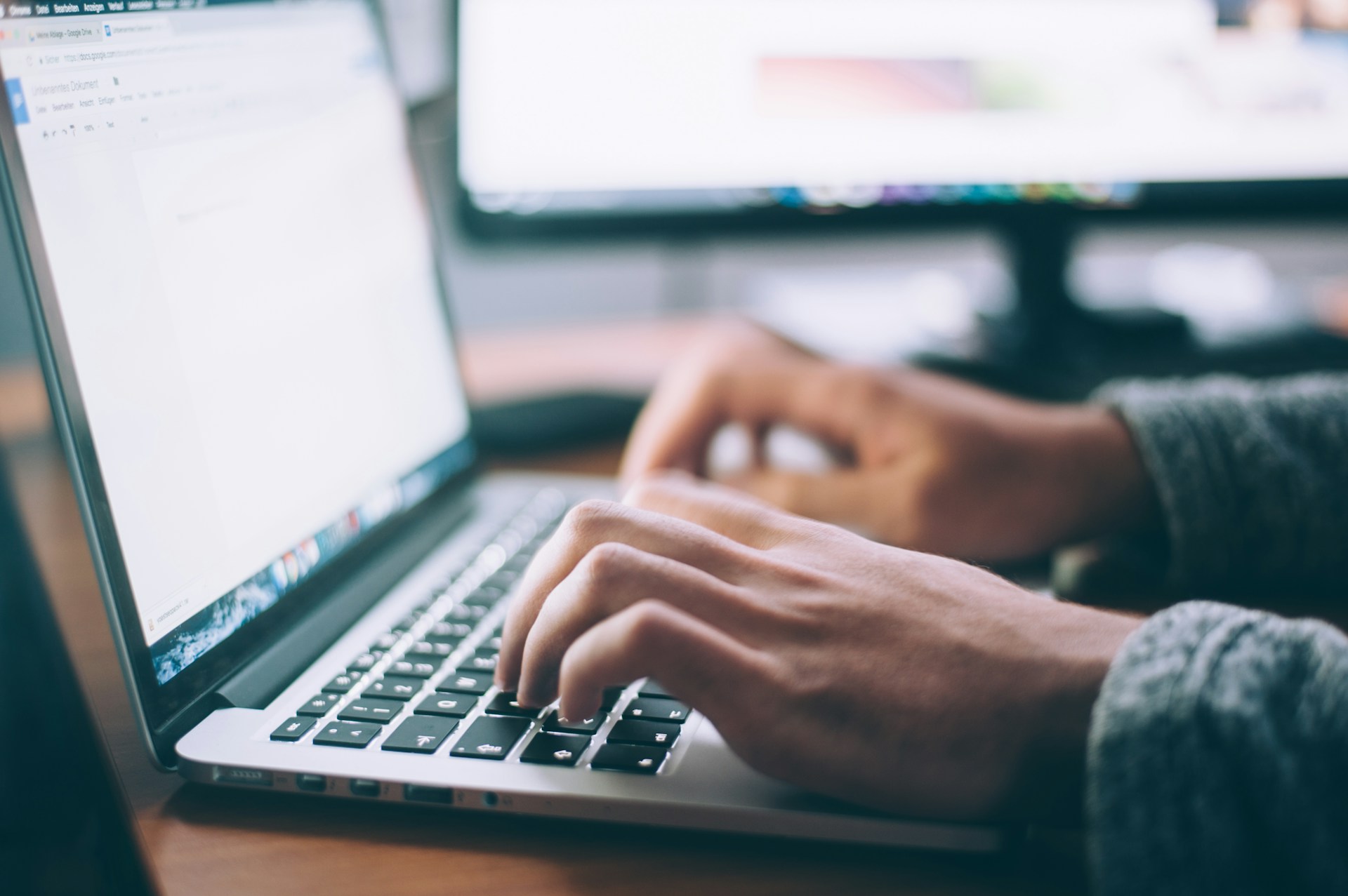 A laptop with an opened text editor tool with somebody’s hands typing text.